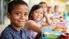 Children smiling at the camera next to their school lunches